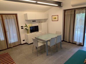A compact living space with a dining table, chairs, a flat-screen TV, a small cabinet, and a framed picture on the wall.