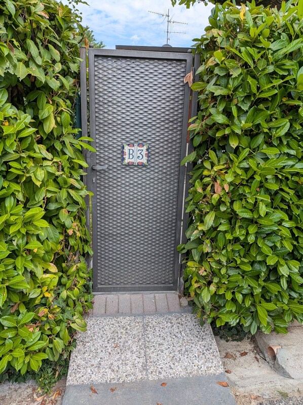 A gated entrance with a textured door, a small sign with 'B3', and a gravel pathway leading to the gate.