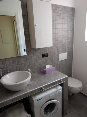 A bathroom with a sink, mirror, cabinet, toilet, and a washing machine.