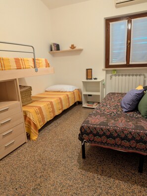 Una habitación tipo dormitorio con literas, un escritorio, una silla, un radiador y una ventana.