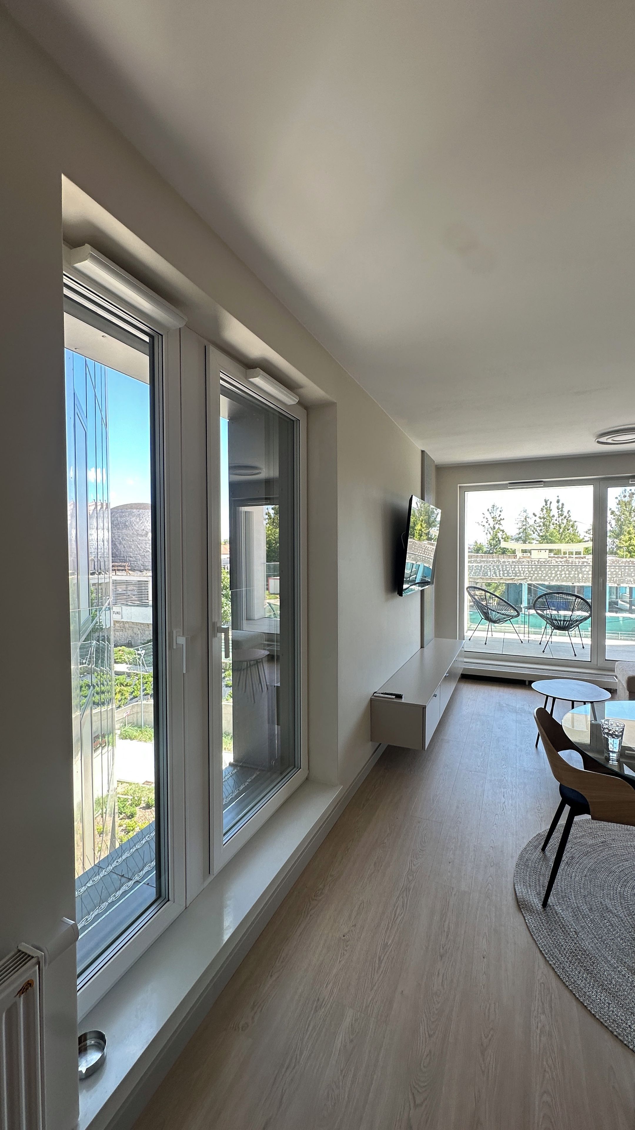 A modern interior with large windows, a flat-screen TV, and a dining area with chairs and a table.