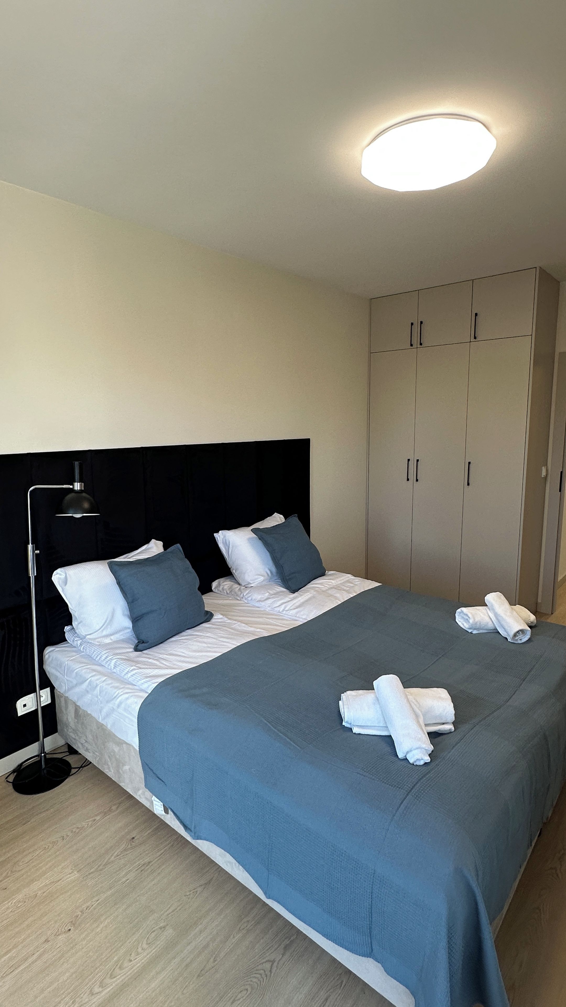 A neatly made bed with pillows, a bedside lamp, and towels on the floor.