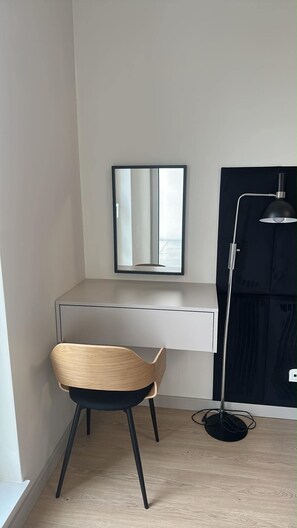 Pelkistetty huone, jossa on työpöytä, tuoli ja lattiavalaisin.