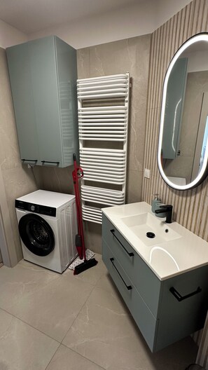 A bathroom with a washing machine, a mirror, and a towel rack.