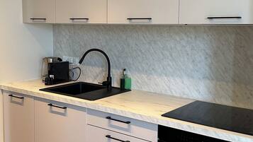Una cocina moderna con armarios blancos, un lavamanos negro y un horno empotrado.