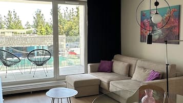 Una sala de estar moderna con una mesa de centro de vidrio, un sofá y una mesa de comedor. Hay un ventanal que ofrece vistas al exterior.