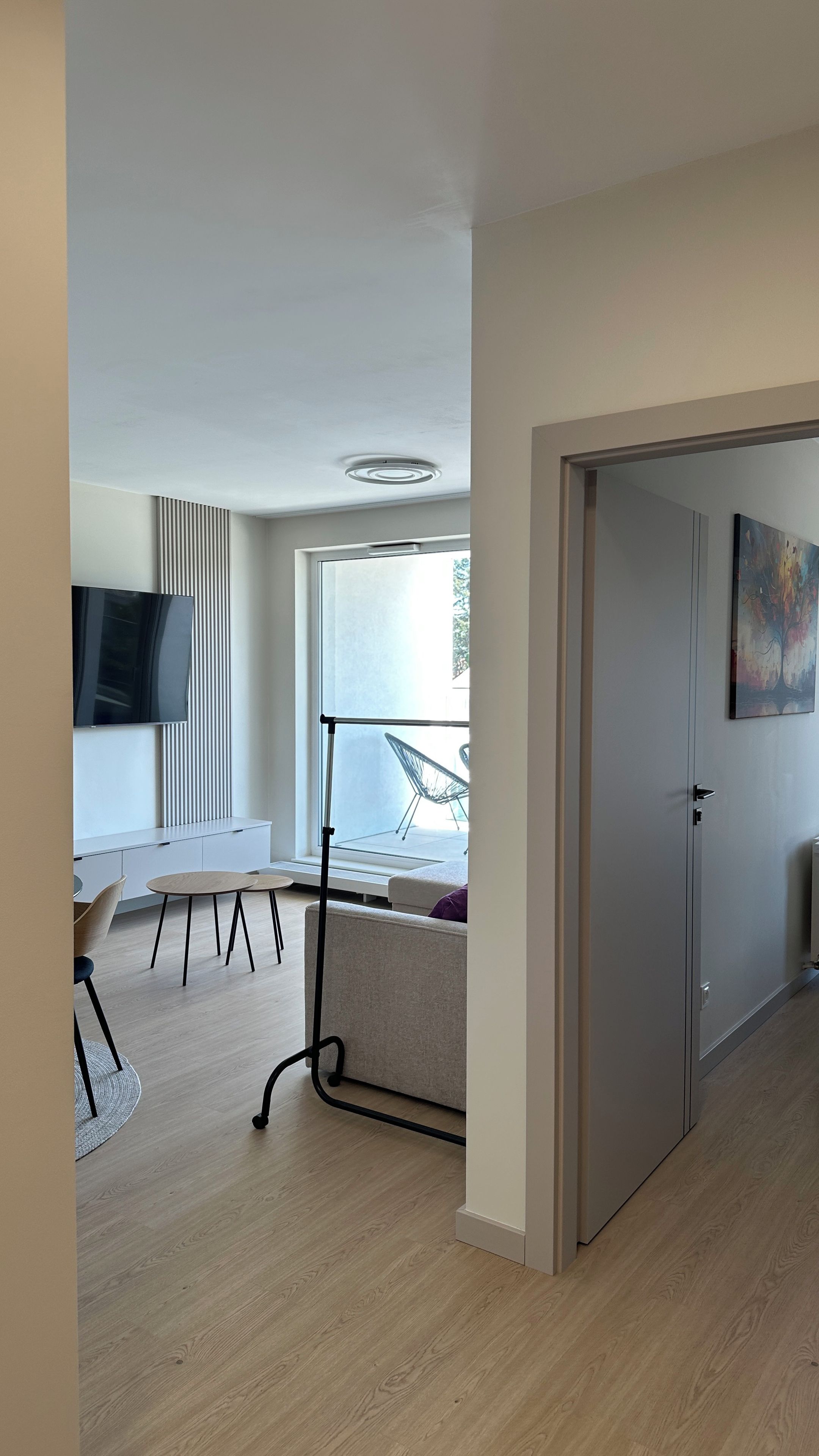 En moderne stue med et fladskærms-tv, en sofa, et spisebord med stole og en balkon med en stol.