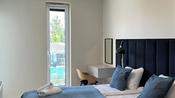 A modern hotel room with a large bed, a desk, and a view of the outdoors.