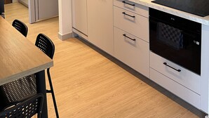 A modern kitchen with white cabinets, a black countertop, and a built-in oven. There is a dining area with a wooden table and chairs.