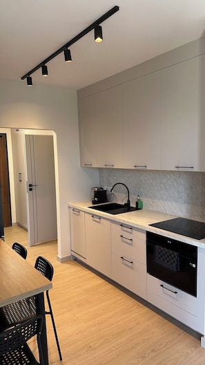 A modern kitchen with white cabinets, a black countertop, and a built-in oven. There is a dining area with a wooden table and chairs.