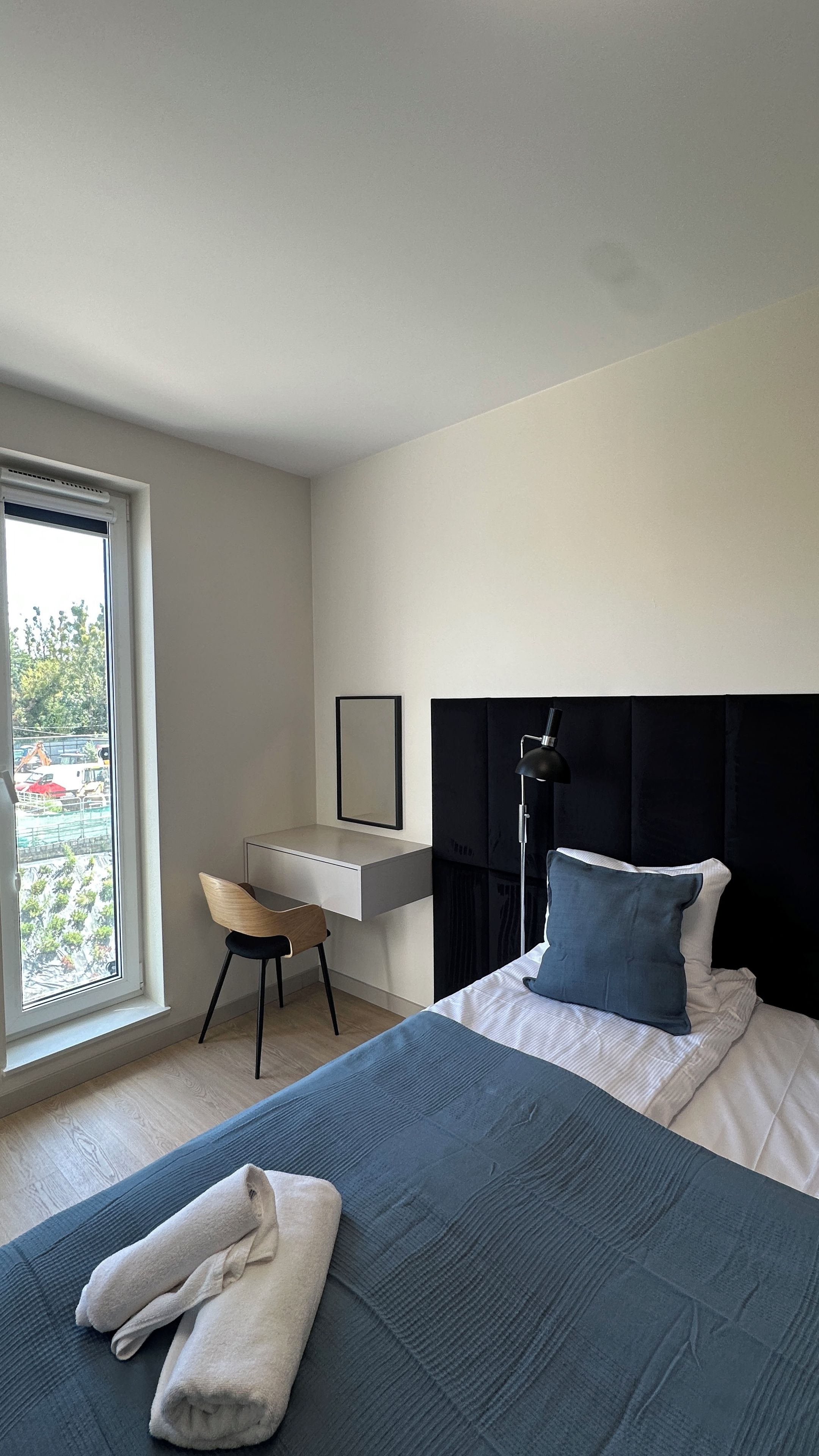 A modern hotel room with a bed, a desk, a chair, and a large window.