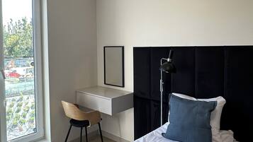 A modern hotel room with a bed, a desk, a chair, and a large window.