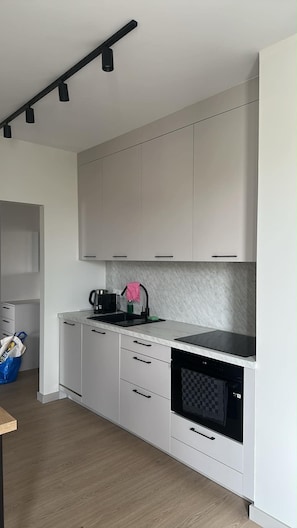 Moderni keittiö, jossa on valkoiset kaapit, musta työtaso, kahvinkeitin ja mikroaaltouuni.