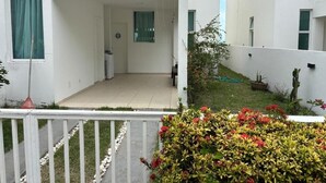 A white building with a small garden area, a door, and a window with curtains. - Ipioca Beach House (Maceió)