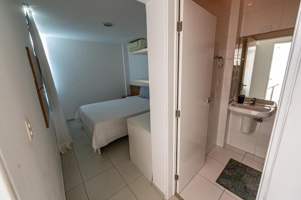 A bedroom with a bed, a bedside table, a wardrobe, and a bathroom with a sink and mirror.