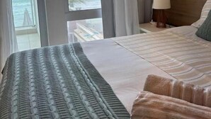 A bedroom with a bed, a nightstand, a lamp, and a view of the ocean. - Ipioca Beach House (Maceió)