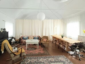 A spacious room with a piano, a sofa with patterned cushions, a dining table with chairs, and a large rug. - Old parish hall in Kvæfjord (Borkenes)