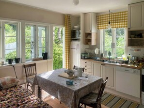 A kitchen with a dining table, chairs, and a window with curtains. - Old parish hall in Kvæfjord (Borkenes)