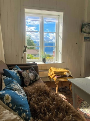 A room with a large window, a sofa with floral cushions, a small table, and a rug.