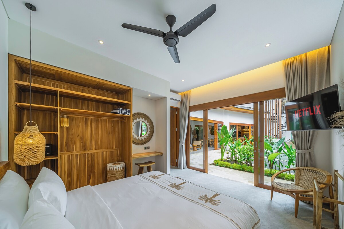 Ein Schlafzimmer mit einem Bett, einem Deckenventilator, einem Fernseher, einem Holzschrank und Blick ins Freie.
