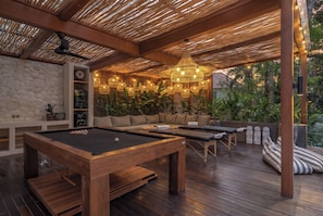 Ein Billardtisch, eine Holzdielen-Terrasse und ein Außenbereich mit Sitzgelegenheiten, einer Steinwand und Pflanzen.