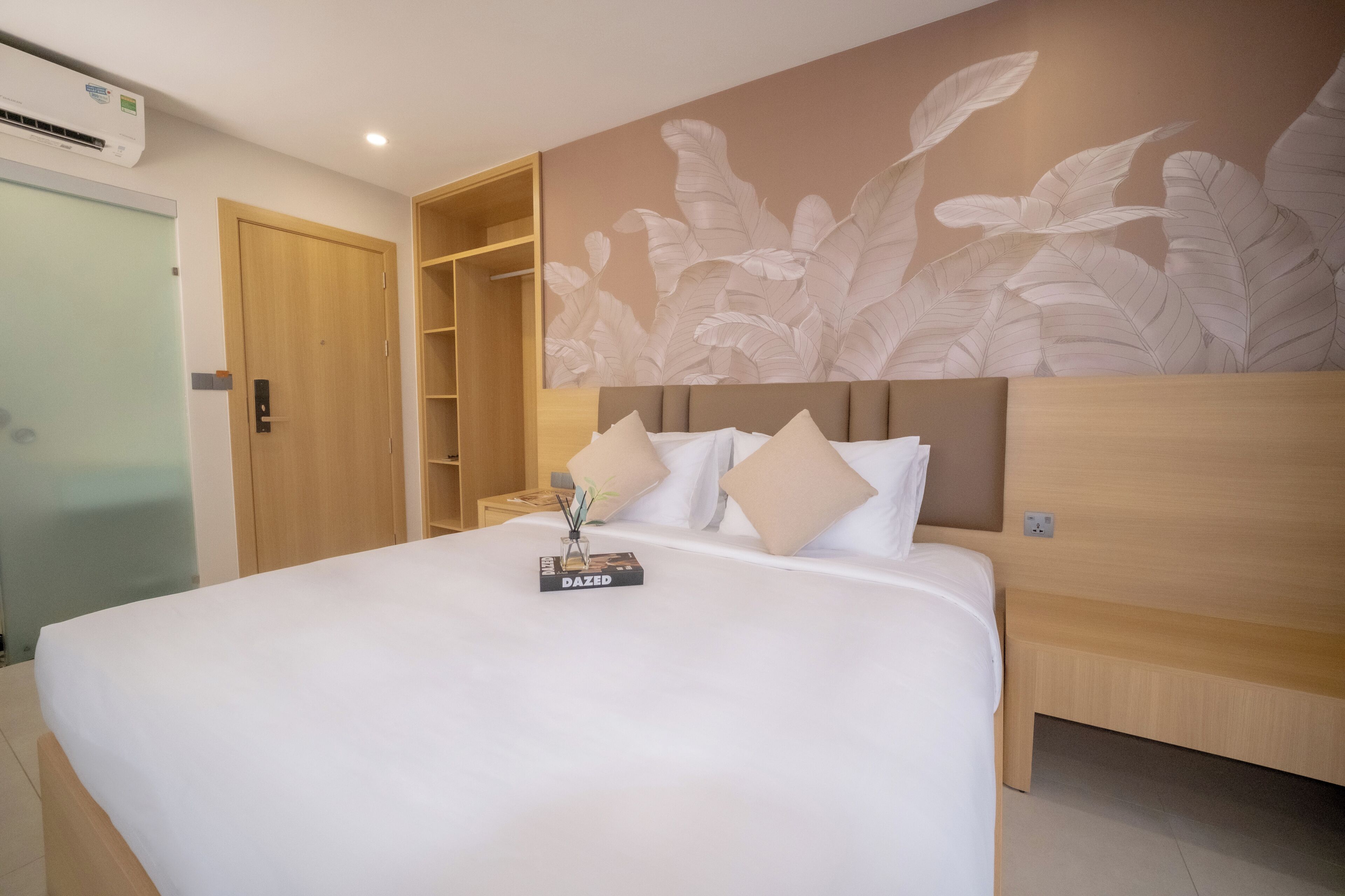 A hotel room with a large bed, a wooden wardrobe, a built-in shelf, and a wall with a leaf pattern.