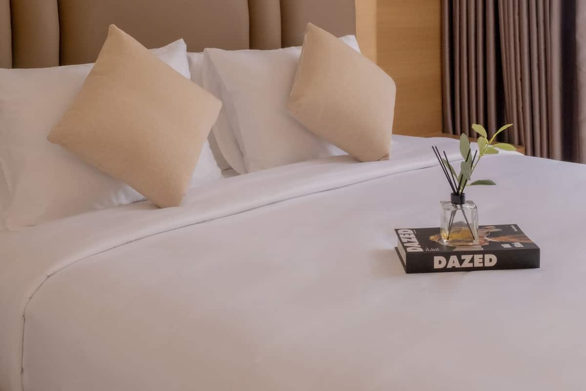 A hotel room with a large bed, a headboard with a leaf pattern, and a vase with a plant on the bed.