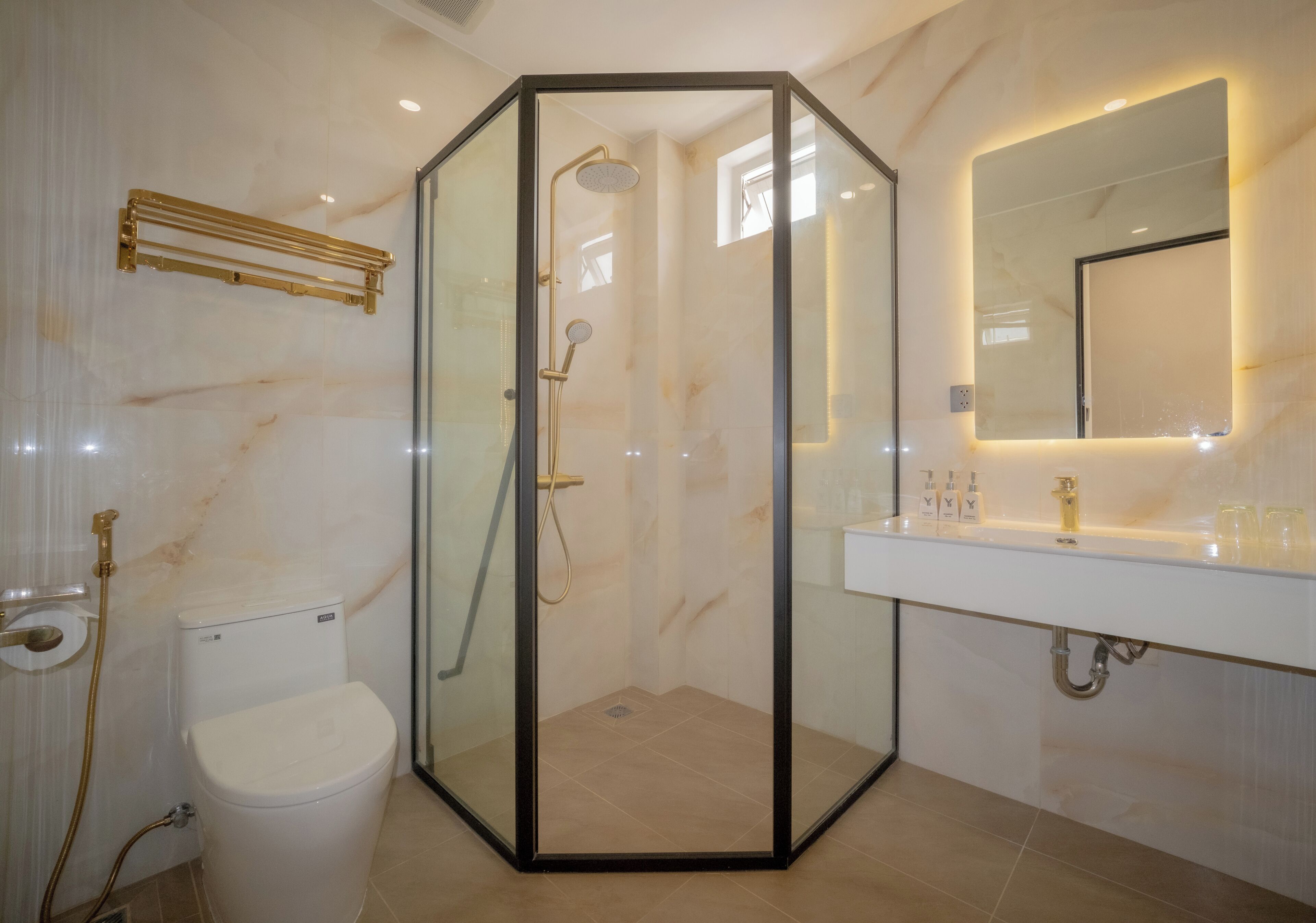 Un baño con ducha de vidrio, inodoro, lavamanos con espejo y artículos de aseo en la encimera.