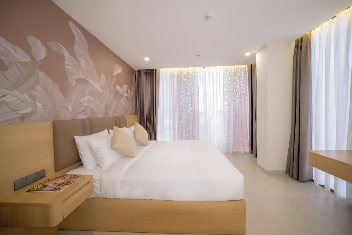 A modern hotel room with a large bed, a nightstand, a wall-mounted TV, and a window with curtains.