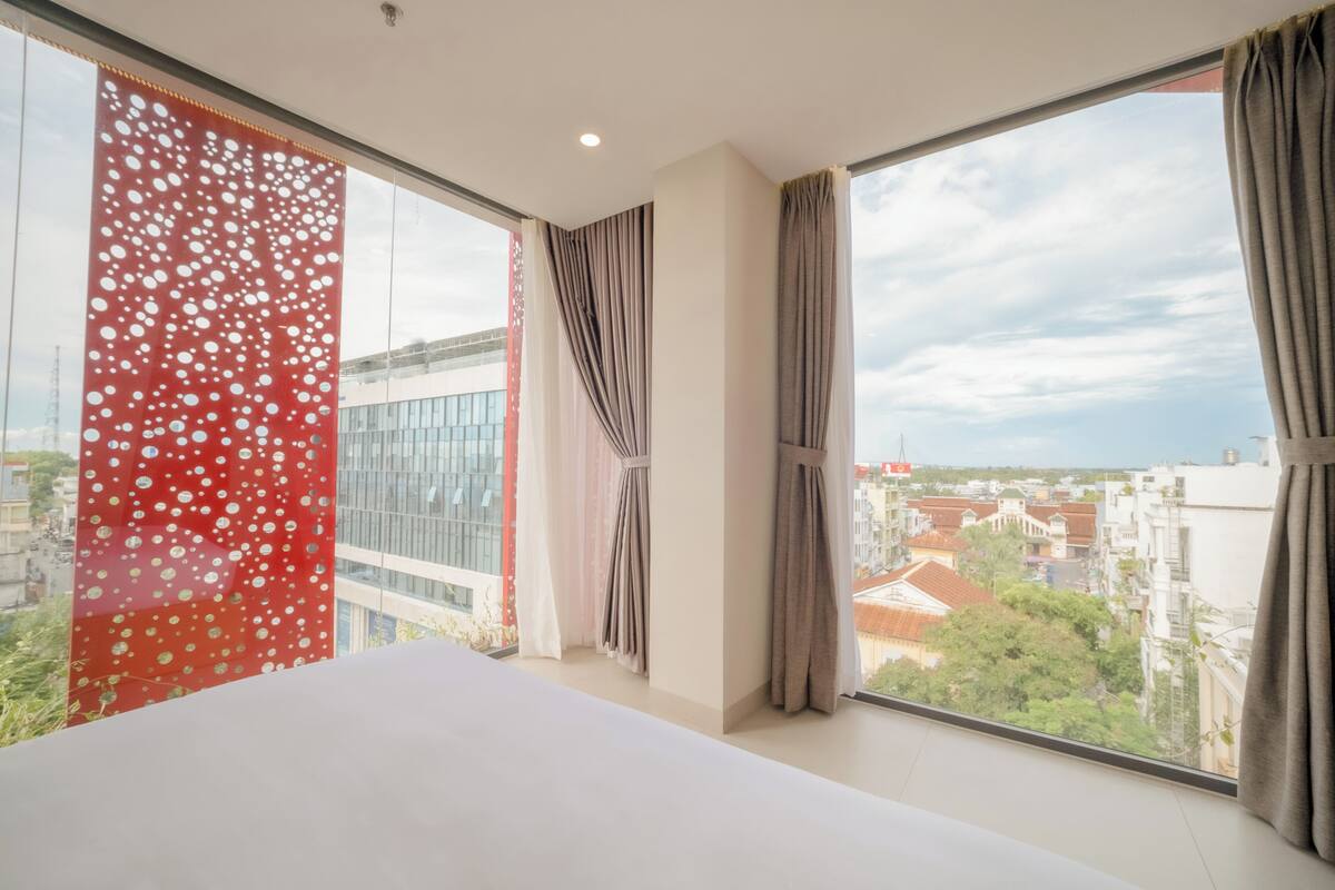 A hotel room with a large window, a bed, and curtains.