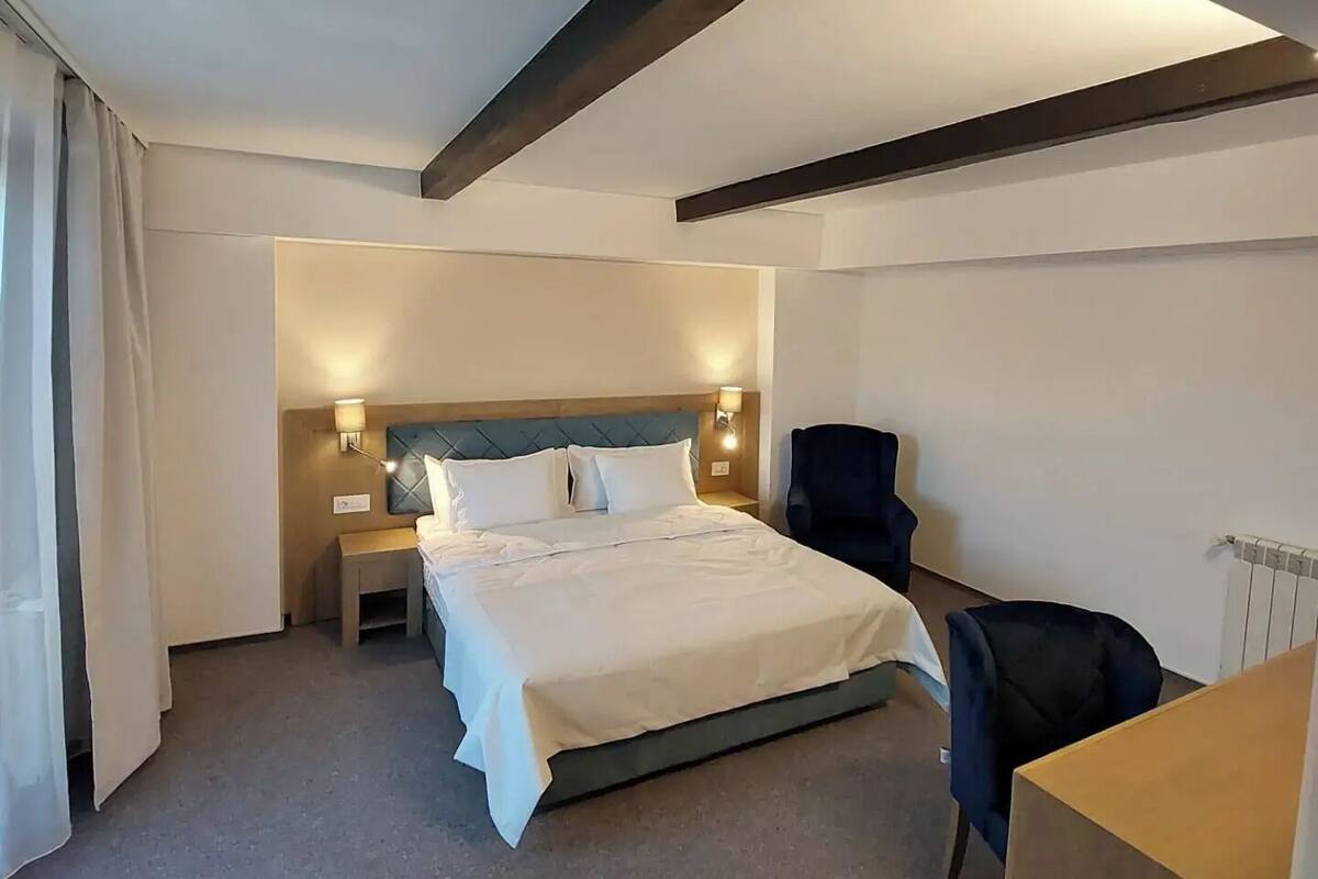 A hotel room with a bed, bedside tables, a chair, and a desk.