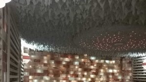 Une pièce avec un mur à texture, deux fauteuils à bascule en bois, un banc et un plafond orné d’un éclairage simulant un ciel étoilé.