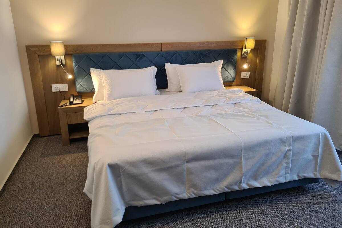 A hotel room with a bed, two bedside tables, a telephone, and wall-mounted lamps.