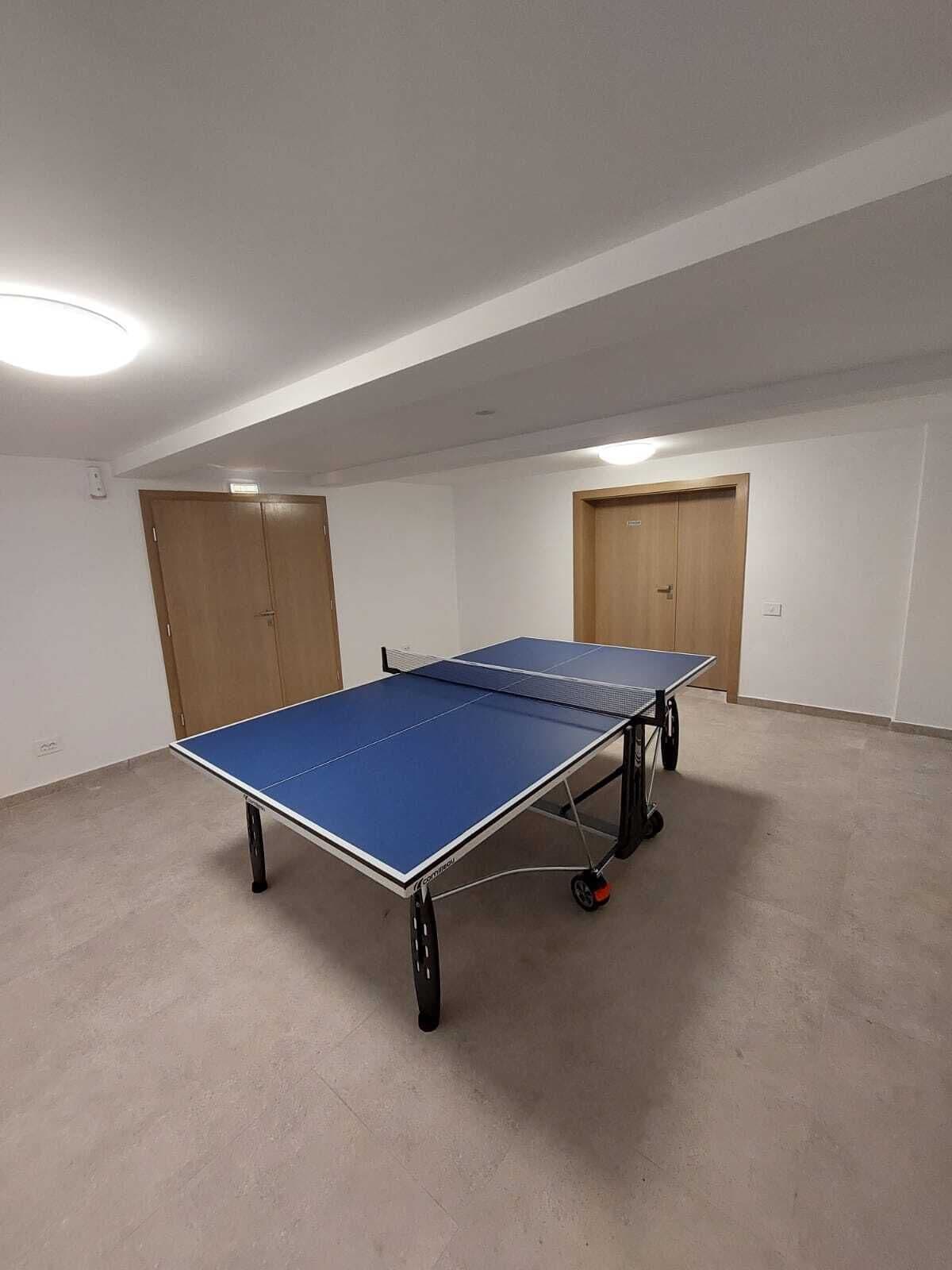 A room with a ping pong table, two doors, and a light fixture on the ceiling.