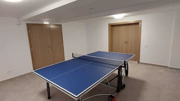 A room with a ping pong table, two doors, and a light fixture on the ceiling.