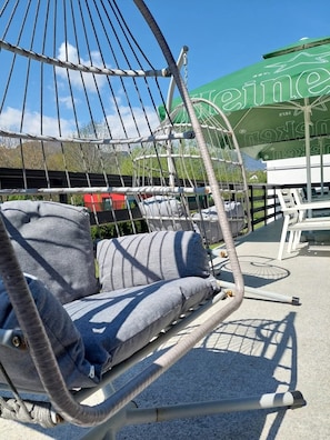 Un sillón hamaca con cojines grises, un paraguas verde y una señal con la palabra 'Leine' al fondo.