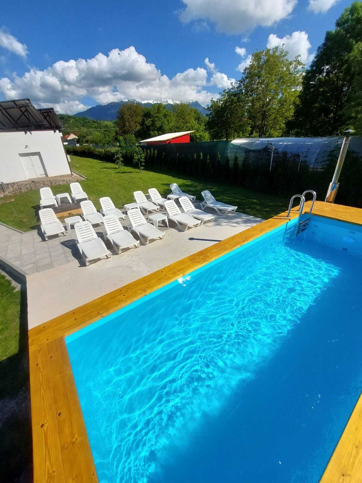 A swimming pool with sun loungers, a wooden deck, and a view of mountains in the background.
