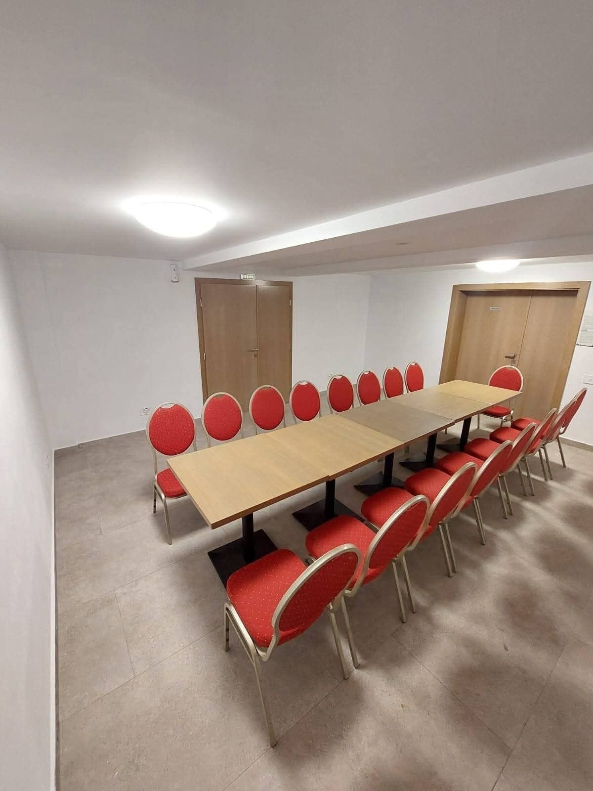 Un salón de conferencias con una larga mesa y sillas rojas, paredes blancas y piso de baldosas.