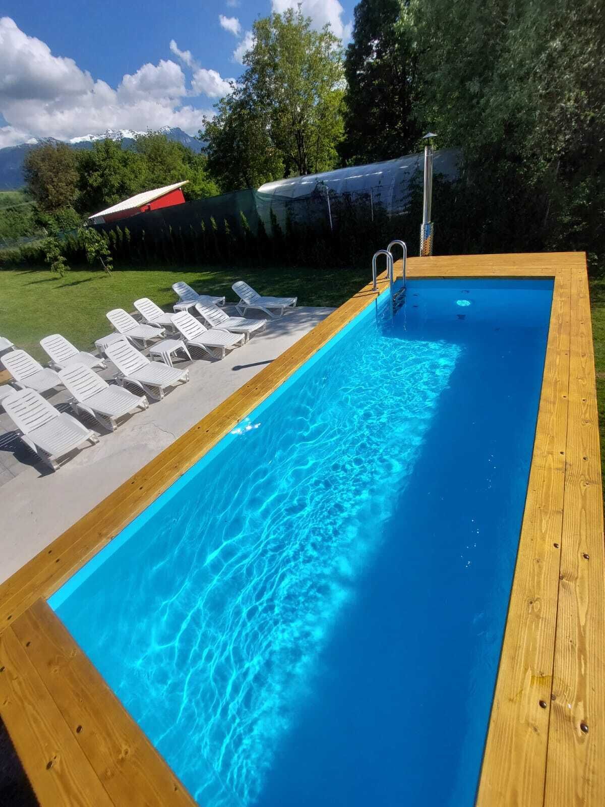 A rectangular swimming pool with a wooden deck and white lounge chairs.