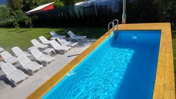 A rectangular swimming pool with a wooden deck and white lounge chairs.