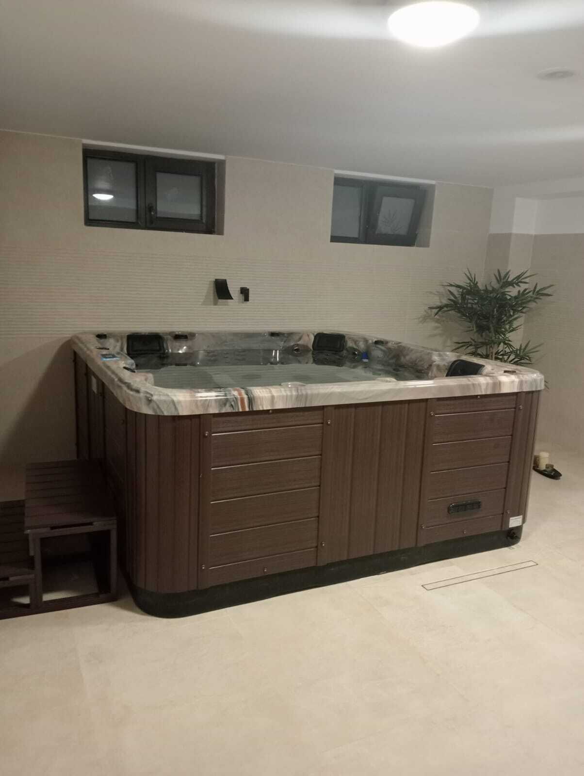 Un espacio tipo spa con un amplio jacuzzi, paneles de madera y una pequeña zona de estar.