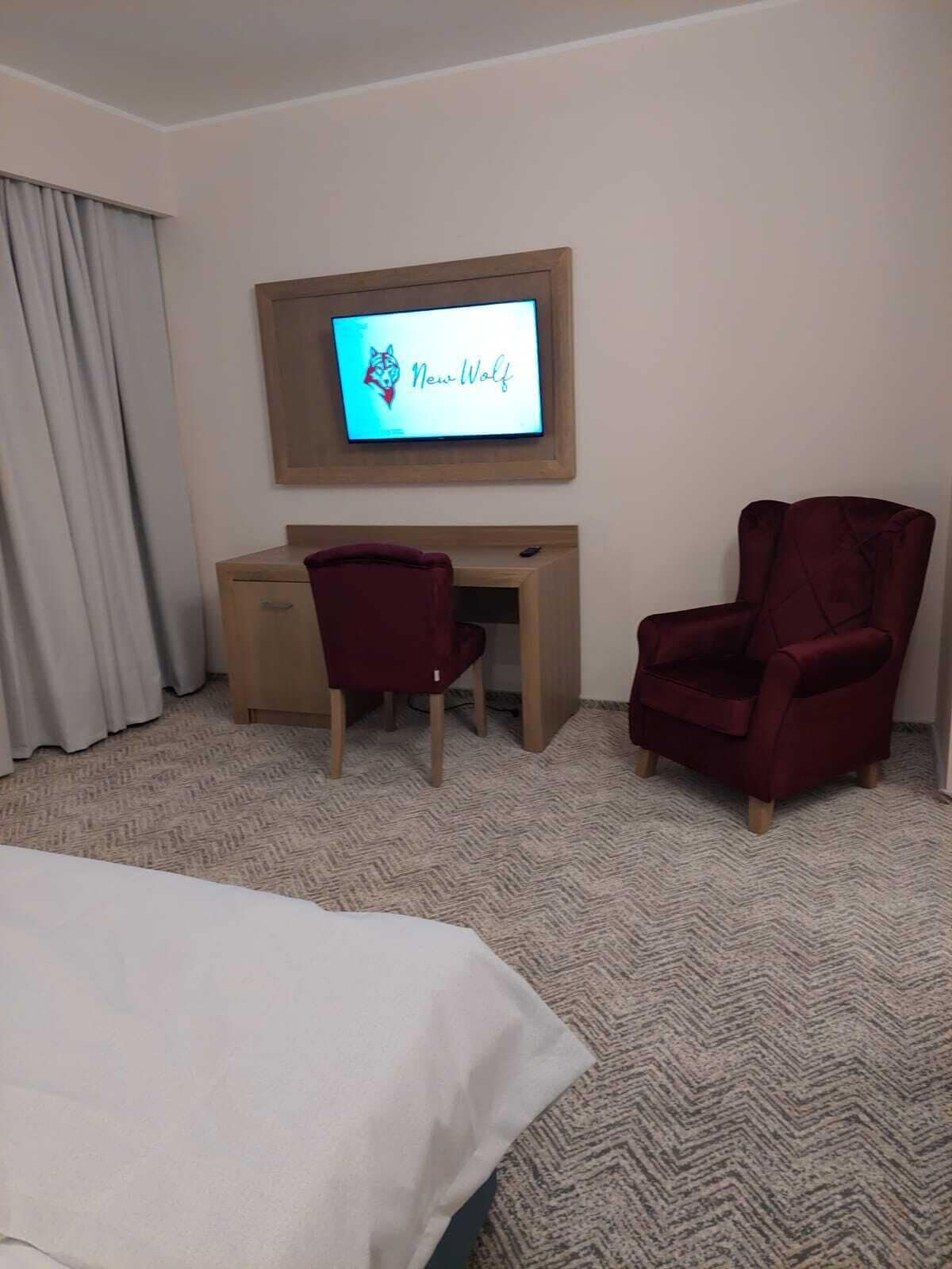 A hotel room with a bed, a desk, two chairs, a TV on the wall, and a carpeted floor.