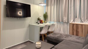 A modern living room with a flat-screen TV, a dining area with a table and chairs, a grey sofa, and a large window with curtains. - SmartLiving Central Apt 8 (Thessaloniki)