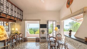 A room with a tiled floor, wooden furniture, a television, and a view of greenery outside.