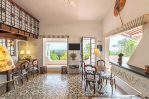 A room with a tiled floor, wooden furniture, a television, and a view of greenery outside. - Villa Bellavista - Oasis with Pool, surrounded by greenery and Breathtaking Sunrises (Carloforte)