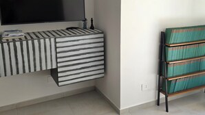 Una habitación moderna con una televisión de pantalla plana montada en la pared, un escritorio a rayas con cajones y una estantería con libros verdes.