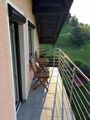 A balcony with a table and chairs, a view of a green landscape, and a building with a beige exterior. - Spacious Alpine Retreat | 3BR, 2BA & Wood-Fired Sauna (Kobarid)