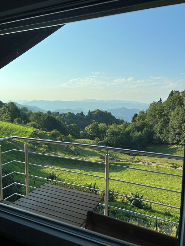 A balcony with a view of a green landscape and distant mountains. - Spacious Alpine Retreat | 3BR, 2BA & Wood-Fired Sauna (Kobarid)