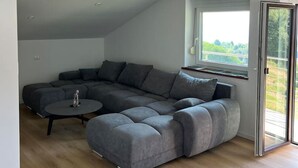 En modern lägenhet i loftstil med en modulsoffa, ett litet runt bord och ett stort fönster med utsikt.