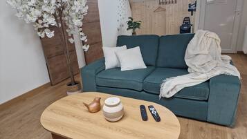 A modern living room with a teal sofa, a round wooden coffee table, and a white orchid plant.